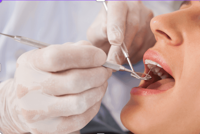 Close-up view of gloved hands holding dental instruments, performing a dental procedure on a patient.