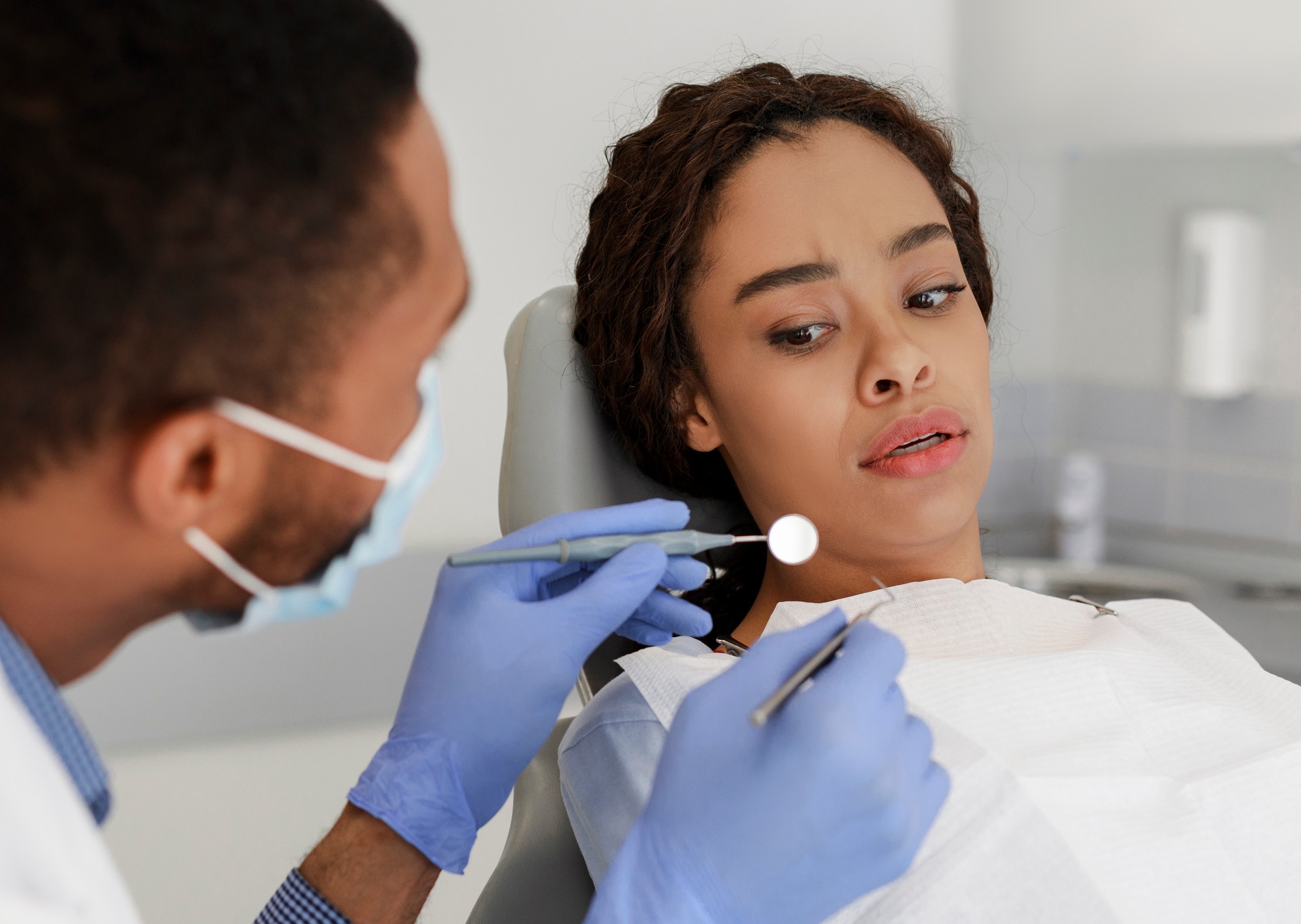 Scared black woman looking at dental tools in doctor hands